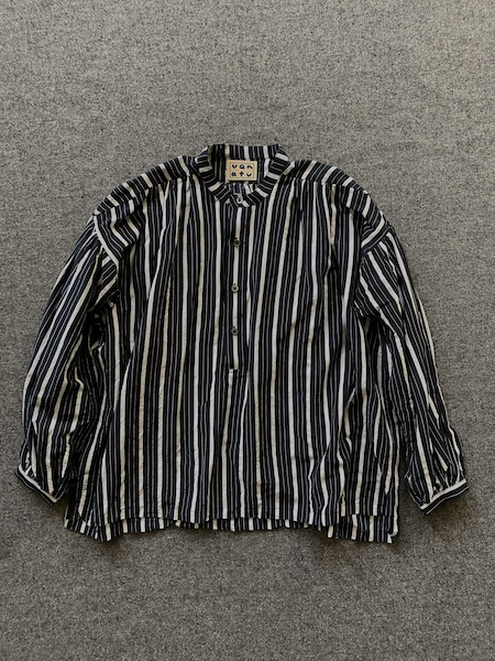 A long-sleeve button-up shirt with vertical black and white stripes, laid flat on a textured gray background.