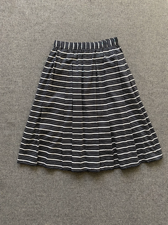 A black and white horizontally striped pleated skirt laid flat on a textured gray carpet.