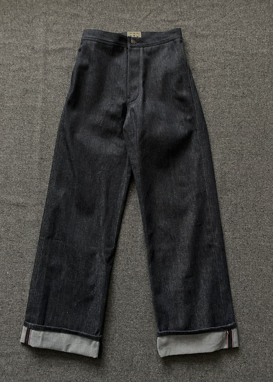 A pair of dark gray washed denim cropped pants with rolled cuffs, laid flat on a textured gray carpet.