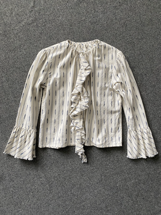 A cream-colored long-sleeve blouse with thin vertical blue stripes, a ruffled tie-neck detail, and ruffled cuffs, laid flat on a textured gray background.