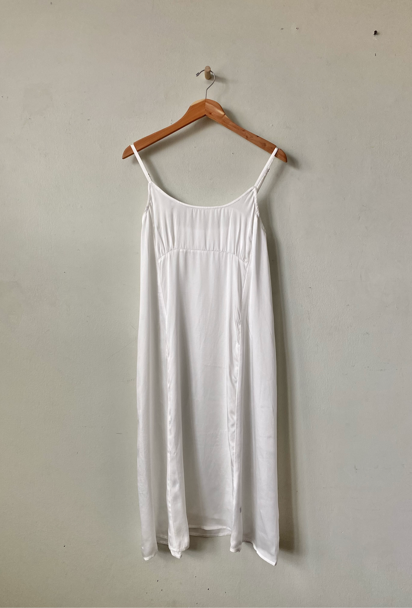 White dress on a wooden hanger against a plain wall