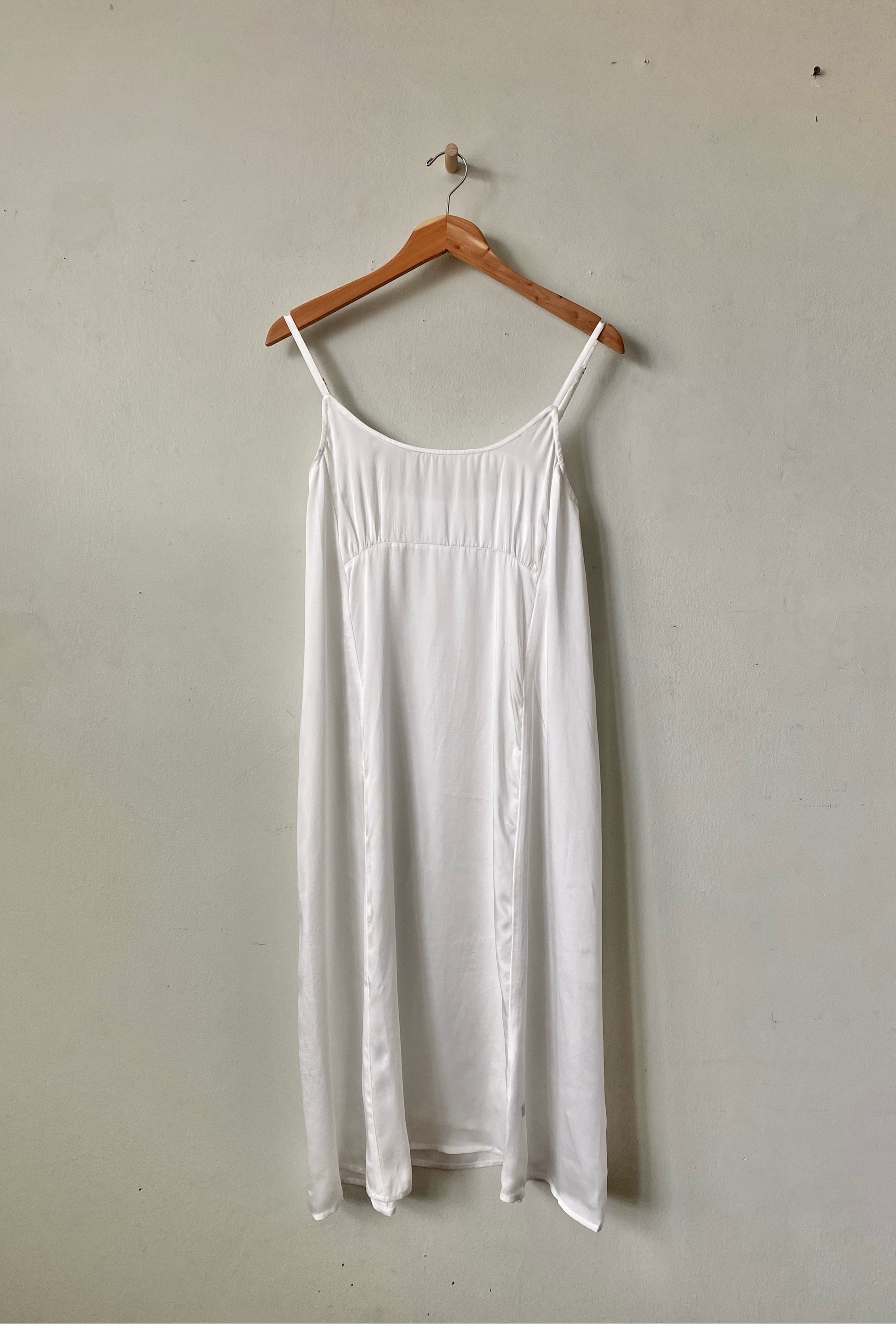 White dress on a wooden hanger against a plain wall