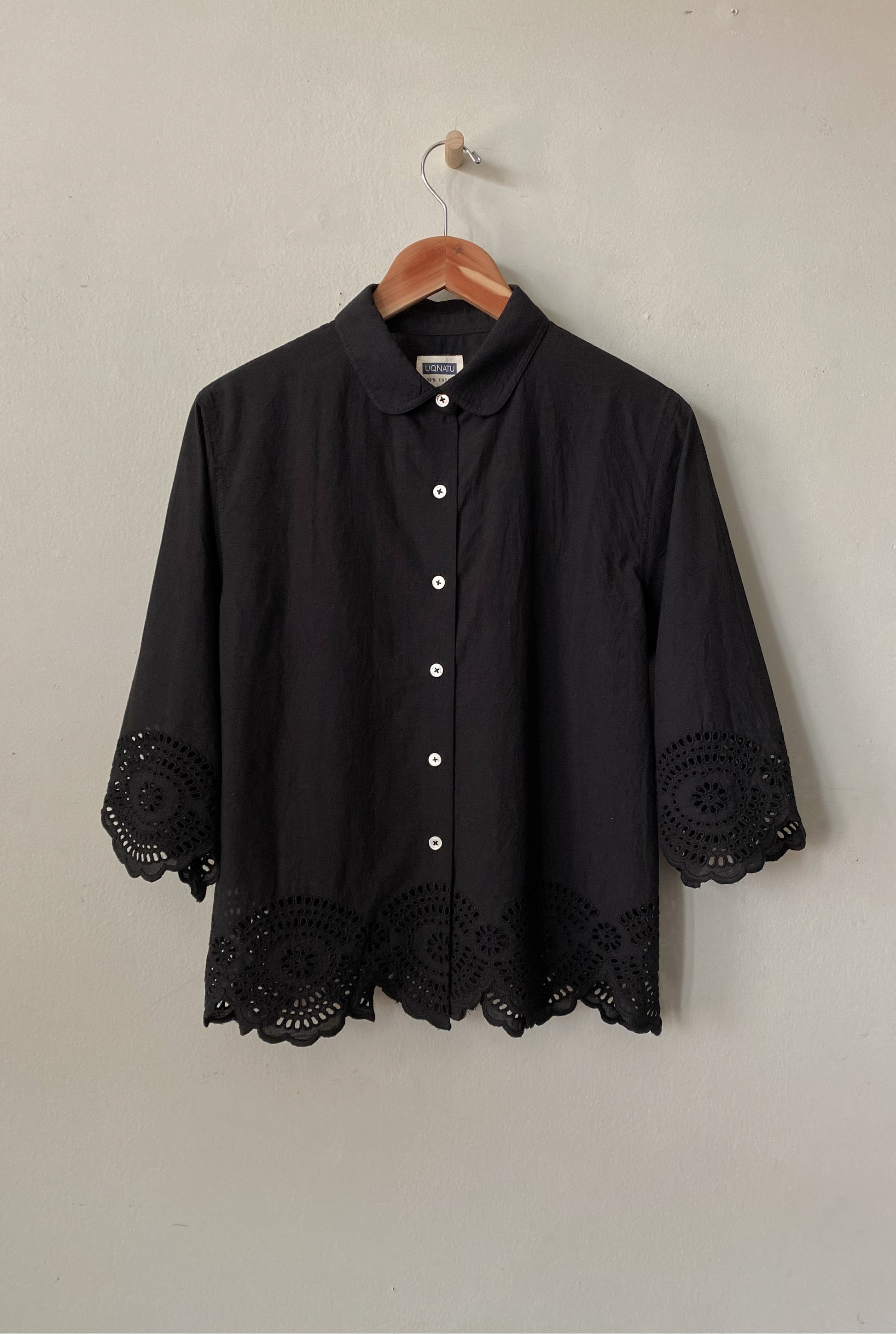 Black shirt with lace details on a hanger against a plain background