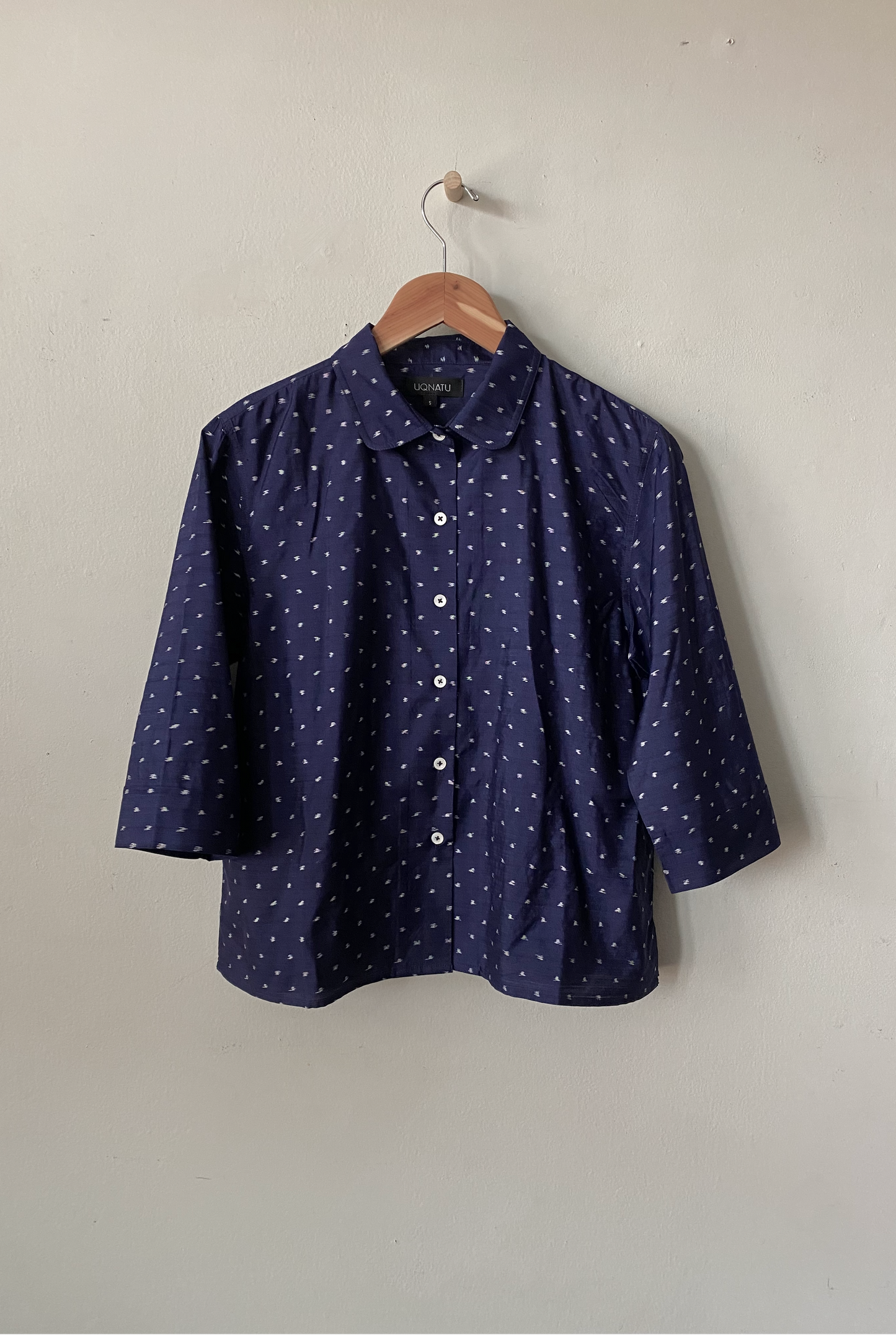 Navy blue shirt with white pattern on a hanger against a plain background