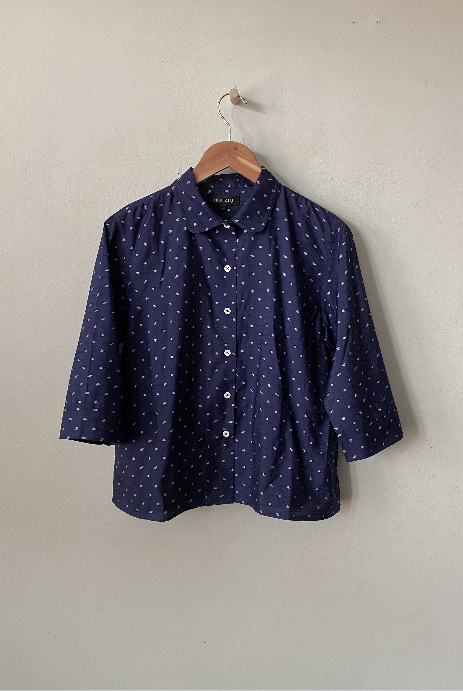 Navy blue shirt with white pattern on a hanger against a plain background
