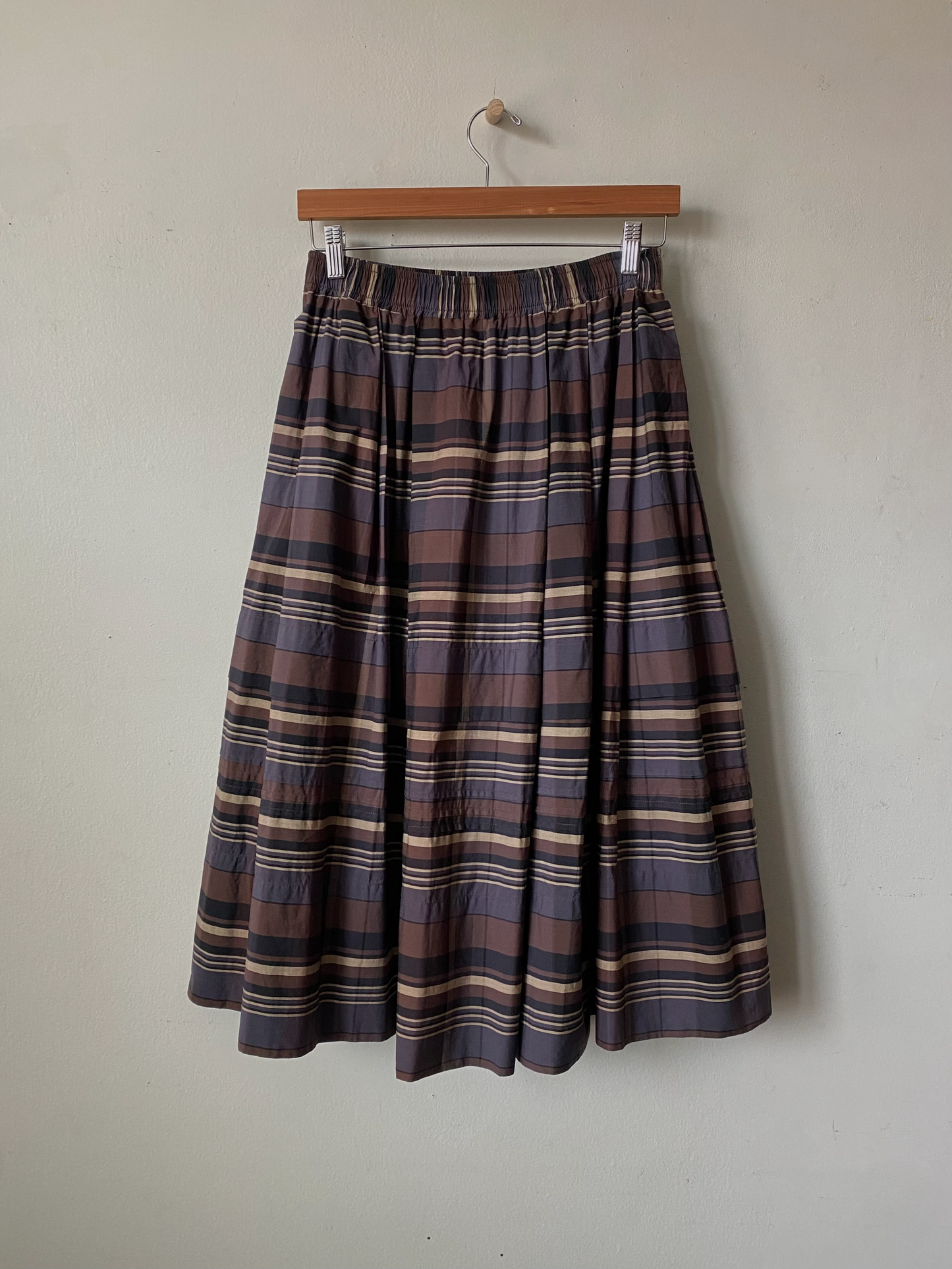 Plaid skirt hanging on a wooden hanger against a plain wall