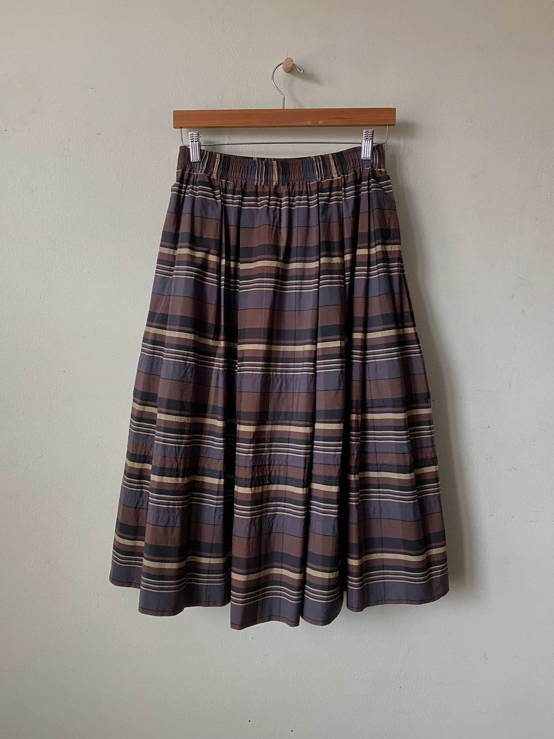 Plaid skirt hanging on a wooden hanger against a plain wall