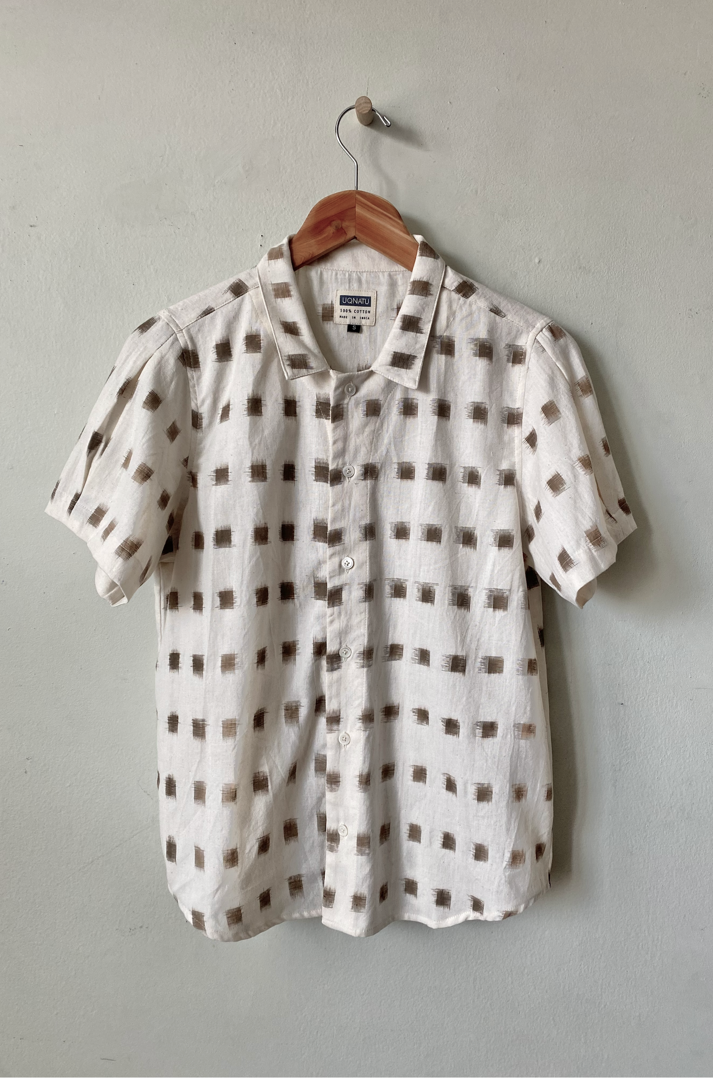 White shirt with brown square pattern on a hanger against a gray wall