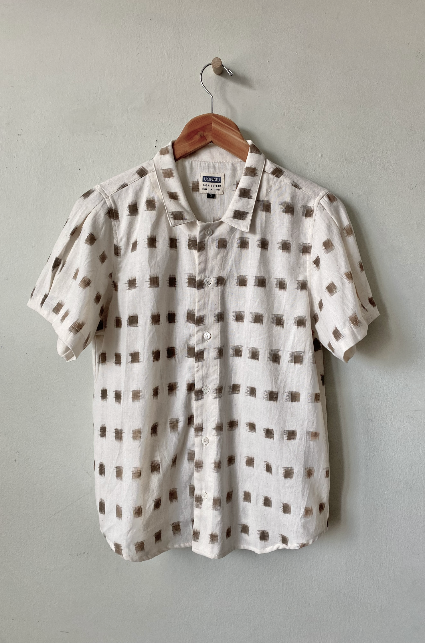 White shirt with brown square pattern on a hanger against a gray wall