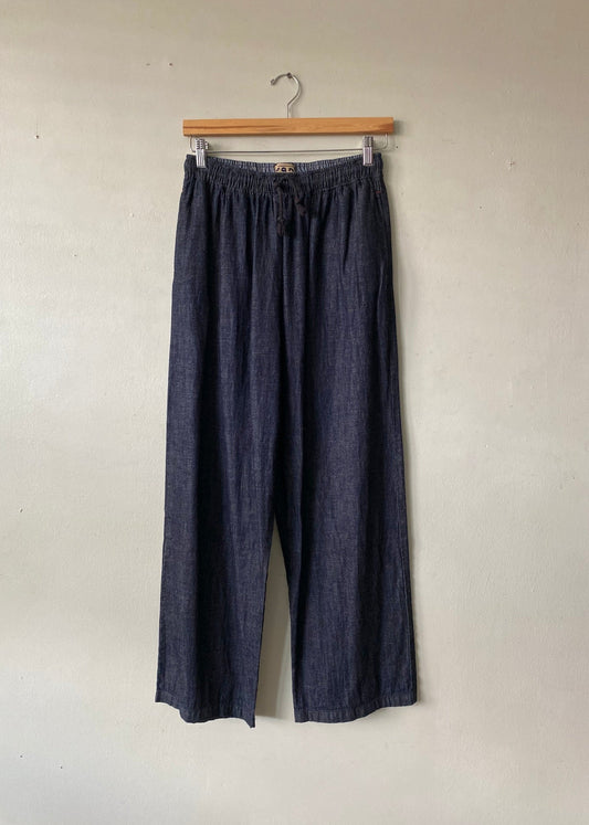 Dark indigo wide-leg pants hanging from a wooden hanger against a plain beige wall.